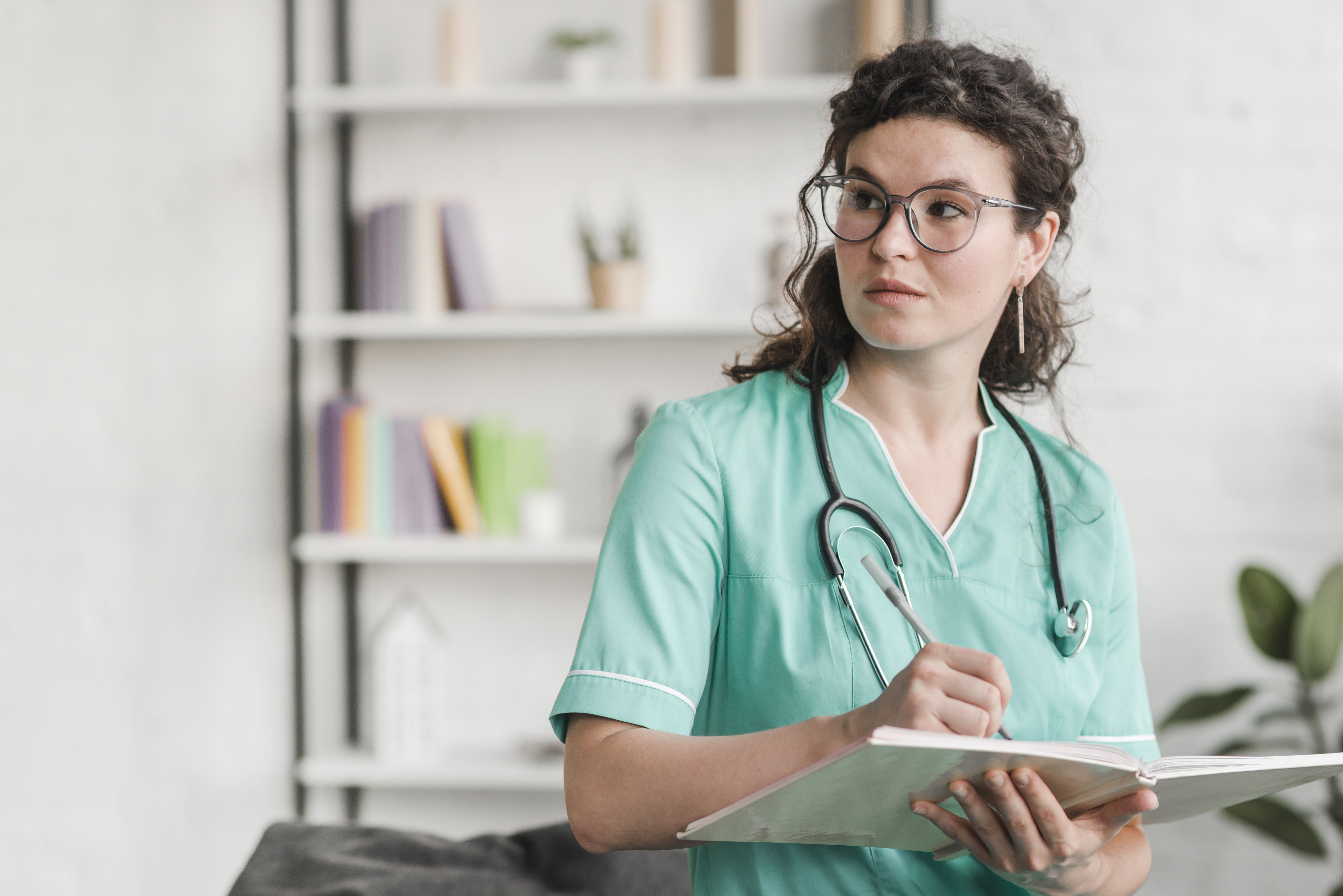 Female-nurse-holding-book-pen-wearing-glasses-looking-away